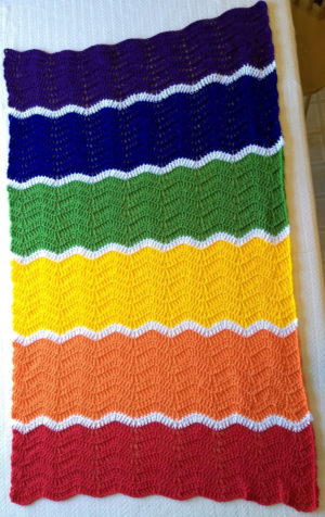 A rainbow ripple crochet blanket laid out on a table
