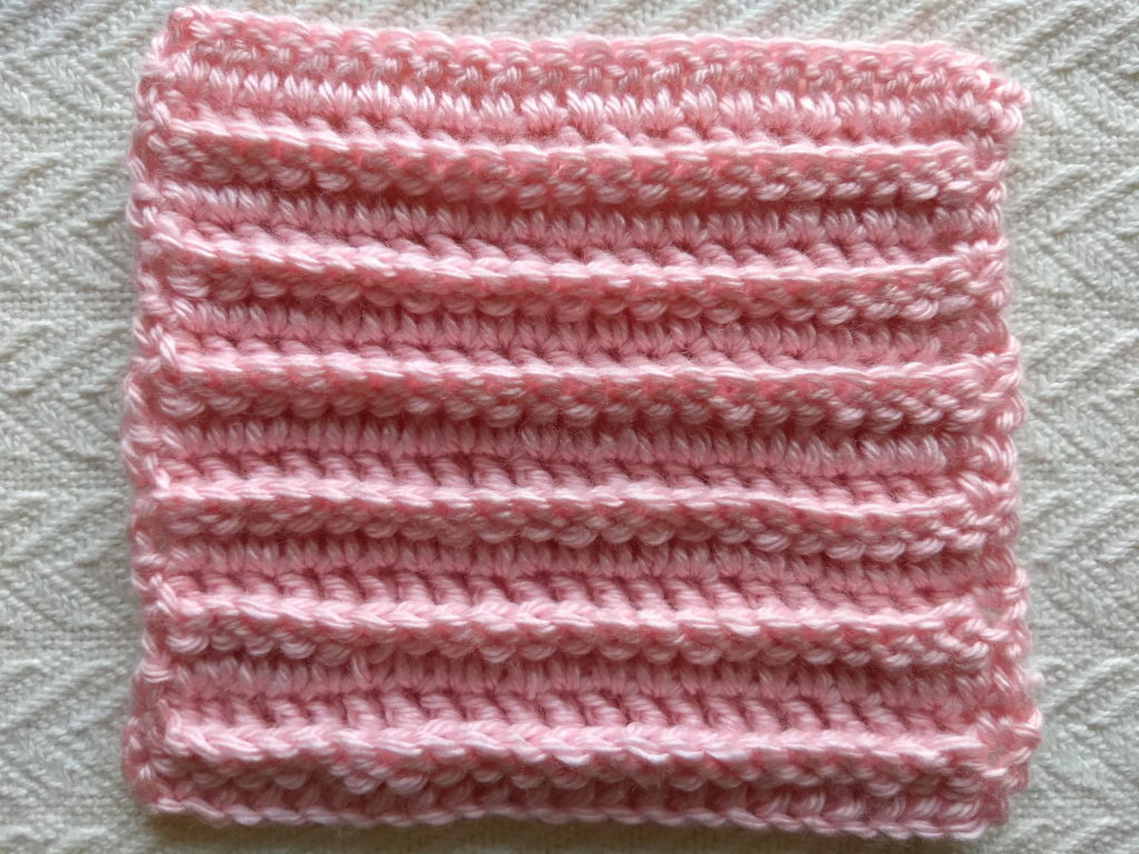 a pink crocheted 6" square made using bpdc, dc, and sc crochet stitches.