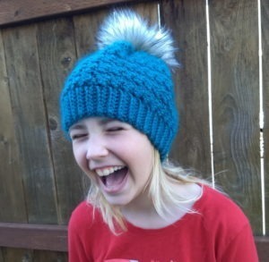 Blond Girl laughing wearing textured crochet hat with pom pom